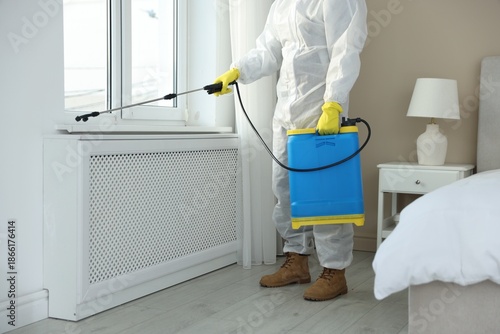 Photos Pest control worker in protective suit spraying insecticide indoors, closeup