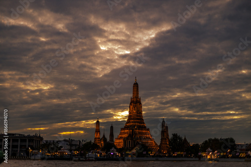 An abstract, blurred background of nighttime lights along the Chao Phraya River in Bangkok, with Wat Arun, a popular tourist attraction visited by travelers from around the world, in the background.