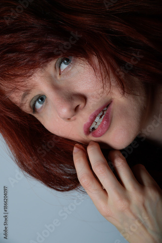 Nahporträt einer jungen Frau mit roten Haaren und hellem Blick vor neutralem Hintergrund. Der direkte Blick und die sanfte Pose vermitteln Natürlichkeit, Nähe und zeitlose Porträtästhetik.