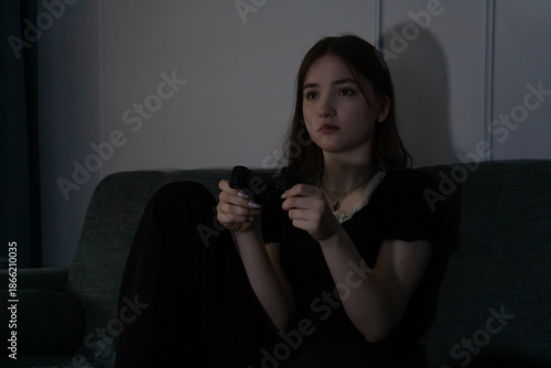 Young girl enjoying a moment of relaxation while holding a video game controller, seated comfortably on a sofa. The scene conveys leisure and entertainment in a cozy setting