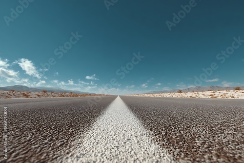 Empty desert highway stretches towards distant mountains under a clear blue sky