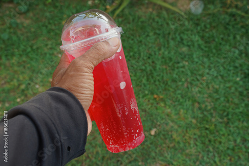Red soda with lime in a plastic cup in my hand