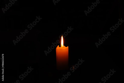 Single burning candle glowing in the dark. Atmospheric minimalist photography of a bright flame against a black background, symbolizing hope, spirituality, mourning, or peaceful silence