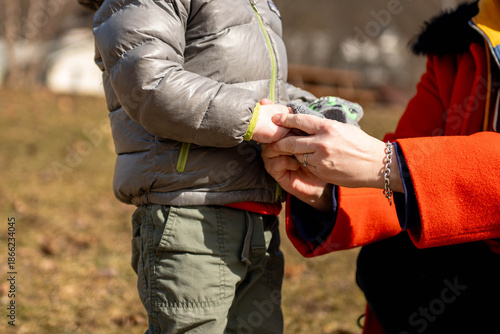 Obraz na plátne Close-up of a caring mother in red wool coat assisting her child in gray winter jacket to put on warm mittens