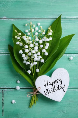 Lily of the valley bouquet with heart-shaped birthday note on mint wooden background