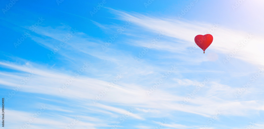 Fototapeta premium Red heart shaped balloon flying in the sweeping blue sky, romantic travel background, suitable for St Valentines day