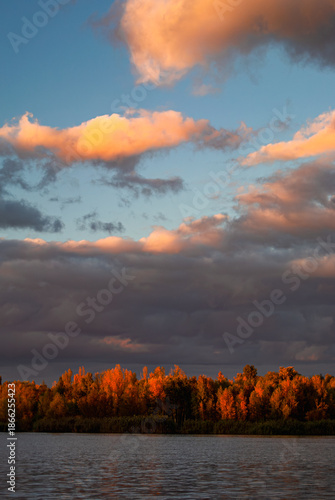 Moody lake landscape with orange foliage and towering evening cloudscape