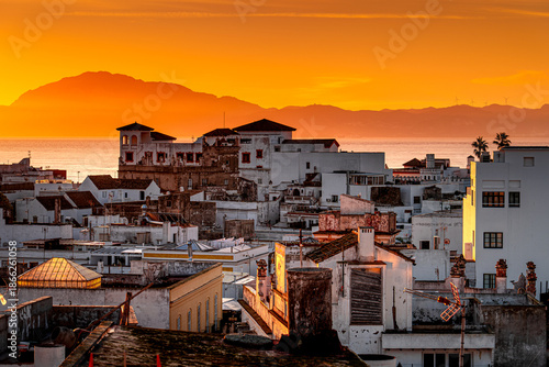Picturesque view of the Moroccan coastline during orange sunrise with buildings on the shore seen from coastal surf town Tarifa in Spain.