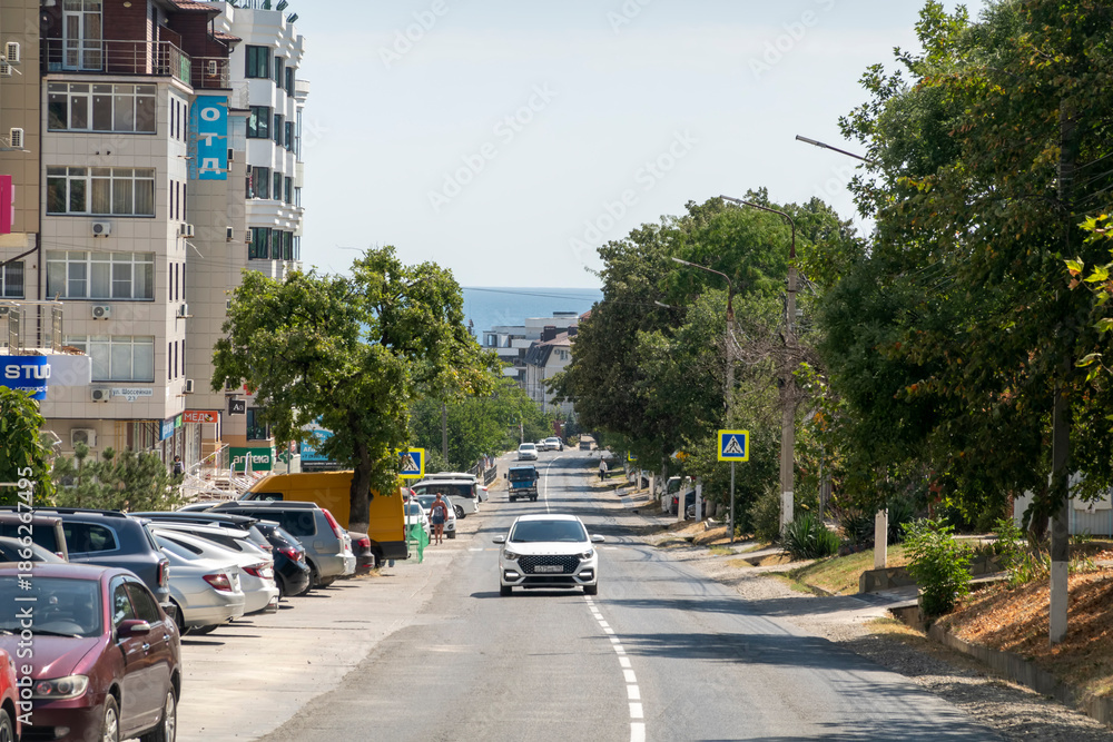 Obraz premium August 24, 2025: Town road in Myskhako, Russia, with cars and residential houses, mountains and the sea in the background, showing everyday life and coastal urban landscape
