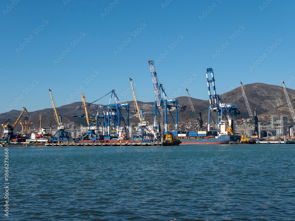 Fototapeta premium August 22 2025 View of Novorossiysk port Russia with cargo ships and cranes on the coastline. Industrial maritime scene on the Black Sea