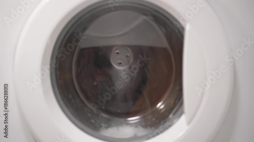 Foamy soap suds churning around shoes in washing machine drum, creating dynamic bubble patterns. Dense white foam envelops footwear during intense cleaning cycle.