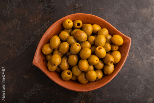 Fresh green olives in ceramic clay bowl on black concrete. Top view, flat lay, close up