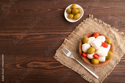 White Mozzarella cheese, with tomatoes and olives on brown wooden, linen textile, top view, copy space.