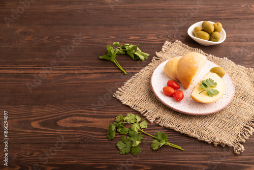 Smoked Mozzarella cheese, with tomatoes and olives on brown wooden, linen textile, side view, copy space.