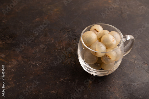 Ripe peeled Longan in glass on black concrete, side view, copy space