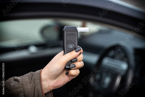 Hand With Manicure Holds Breathalyzer Inside Vehicle. Close-Up Of Sobriety Checking Device.