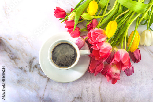 Valentine's day concept; top view for white cup of coffee and bunch of pink, yellow, white tulips on a marble background