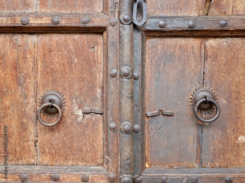 Fotografie BANGKOK, THAILAND – JUNE 15, 2025: A detailed view of two iron ring knockers and metal studs on a traditional wooden door in the Song Wat neighborhood of Bangkok
