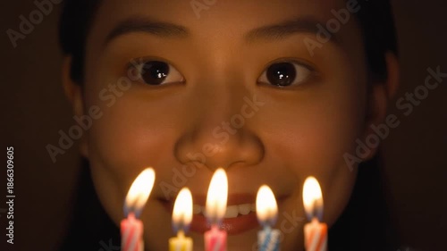 Wallpaper Mural Young Asian girl celebrating her birthday with five lit candles in front of her face, creating a warm glow in a dark room. Torontodigital.ca