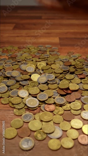 Male hands gathering, counting, and dropping a large pile of shiny Euro coins onto a dark wooden surface, representing wealth and savings