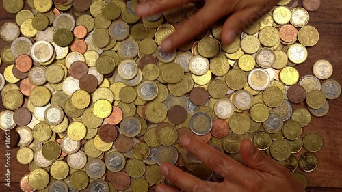 Top-down view of female hands sorting through and counting a large amount of euro coins scattered on a wooden surface, showing wealth