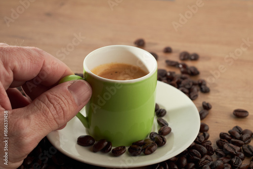 Hand holding green espresso cup with coffee beans on table