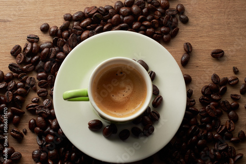 Top view of green espresso cup surrounded by coffee beans