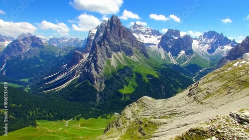 Majestic mountain range with grassy slopes, forested valleys, and snowy peaks under a bright blue sky