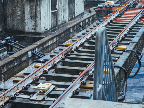 Close-up of modern railway track infrastructure with steel rails, sleepers, sensors, and cabling in an urban transit system, highlighting precision engineering, maintenance, and transportation.