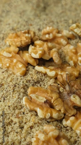 Whole walnut halves poured on crushed walnut kernels flour slow motion vertical macro