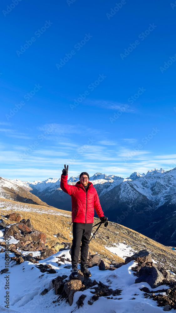 Obraz premium Adventurous man in a vibrant red jacket stands triumphantly atop snowy peaks, embracing mountain serenity and Winter Solstice spirit