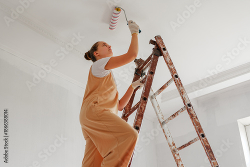 Fotografi A woman is using a paint roller to apply a fresh coat of white paint to the ceil