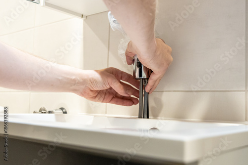 Konstfotografi Person installing a chrome bathroom faucet on a white sink