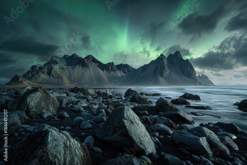 Jagged mountain range under a glowing aurora borealis, foreground rocks and sea