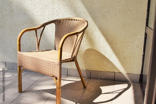 A rattan wicker chair sits on a balcony on a summer day.