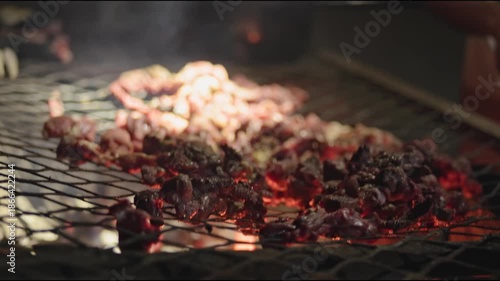 Night time cooking, grilling, and warming fresh goat meat over fire and pot on grill top grate in Africa with Zimbabwe culture, cooks, and people working together to feast on red meats outdoors