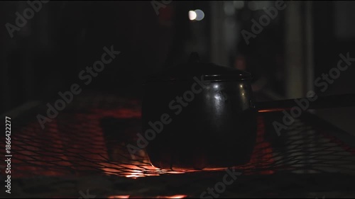 Night time cooking, grilling, and warming fresh goat meat over fire and pot on grill top grate in Africa with Zimbabwe culture, cooks, and people working together to feast on red meats outdoors