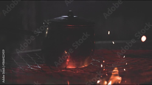 Night time cooking, grilling, and warming fresh goat meat over fire and pot on grill top grate in Africa with Zimbabwe culture, cooks, and people working together to feast on red meats outdoors