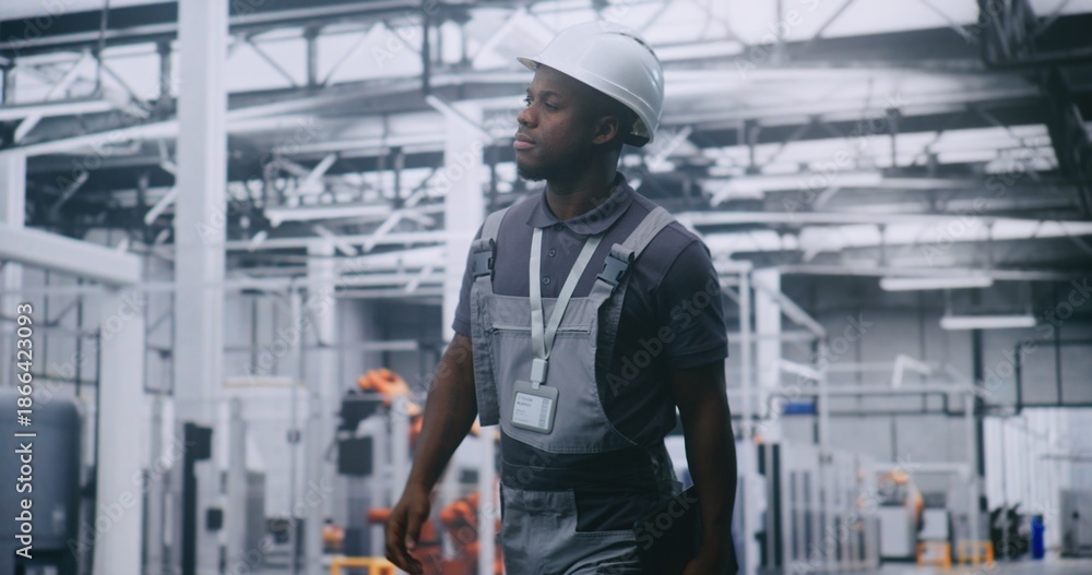 Fototapeta premium African American Male Factory Supervisor Walking Across High Tech Manufacturing Facility, Using Tablet Check Production Data, Assess Machinery Performance and Oversee Automated Industrial Operations.
