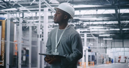 Wallpaper Mural Adult Male Engineer Wearing Safety Helmet, Holding Tablet, and Looking Away to Survey Production Floor. Vast Industrial Interior Emphasizes Strategic Management and Critical On Site Planning. Torontodigital.ca