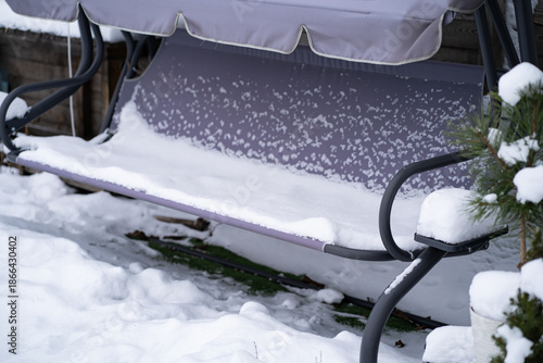 Outdoor garden swing covered with fresh snow in a quiet winter yard. Cold weather, frozen seat and untouched snow create a calm seasonal atmosphere.