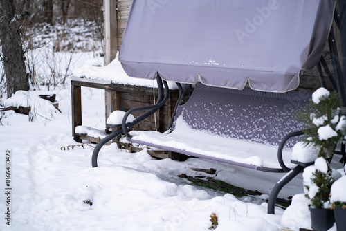 Outdoor garden swing covered with fresh snow in a quiet winter yard. Cold weather, frozen seat and untouched snow create a calm seasonal atmosphere.