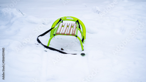 Bright green sled with wooden slats standing on fresh snow. Winter landscape with minimalistic composition, visible pull strap and soft light creating a calm seasonal atmosphere.