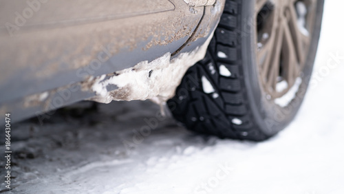 Close-up of a car wheel and dirty body with frozen snow and ice buildup on the fender. Winter driving conditions, icy roads, vehicle maintenance and cold weather effects.