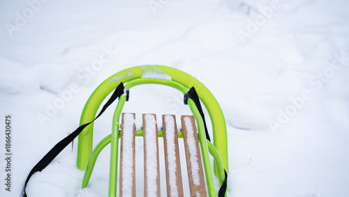 Bright green sled with wooden slats standing on fresh snow. Winter landscape with minimalistic composition, visible pull strap and soft light creating a calm seasonal atmosphere.