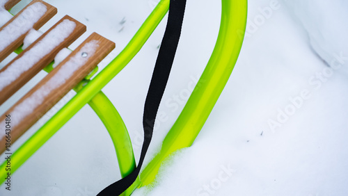 Bright green sled with wooden slats partially covered by snow. Minimalistic winter composition with vibrant color contrast against the white snowy background.