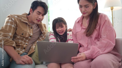 A family sits together on the sofa watching something on a laptop, sharing a relaxed and happy moment in a cozy living room