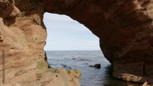 Through a natural arch in Aberdour beach area in Scotland.
