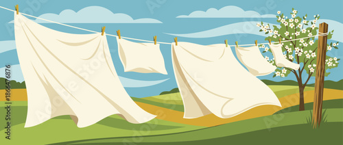 White clean laundry sheets and clothes hanging on a clothesline blow in the wind on a beautiful spring day in a rustic countryside landscape with a blossoming tree