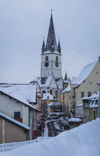 view of frozen downhill street with snow on roofs and main tower on top on cloudy winter day white landscape